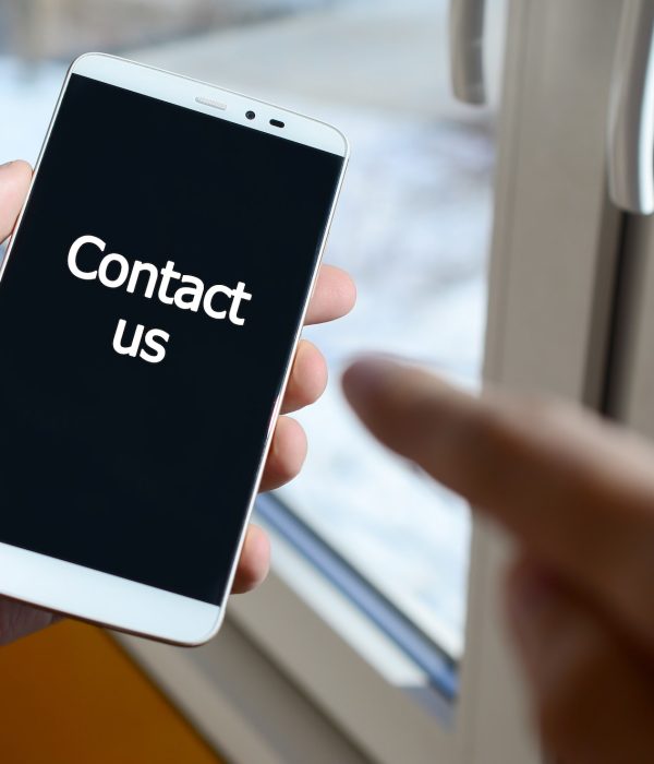 A person sees a white inscription on a black smartphone display that holds in his hand. Contact us