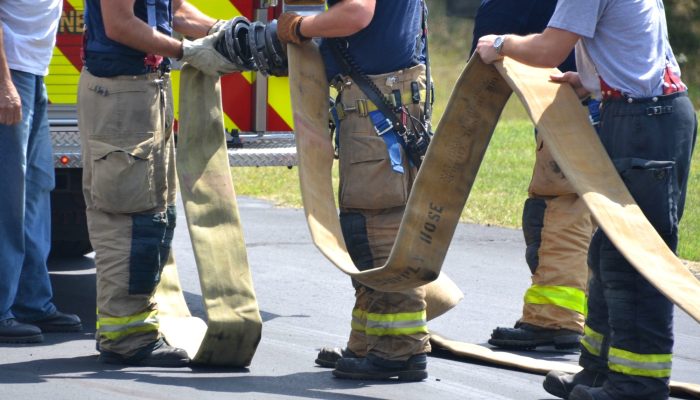 Firefighters helping other firemen with hose next to firetruck. True heroes doing community service.