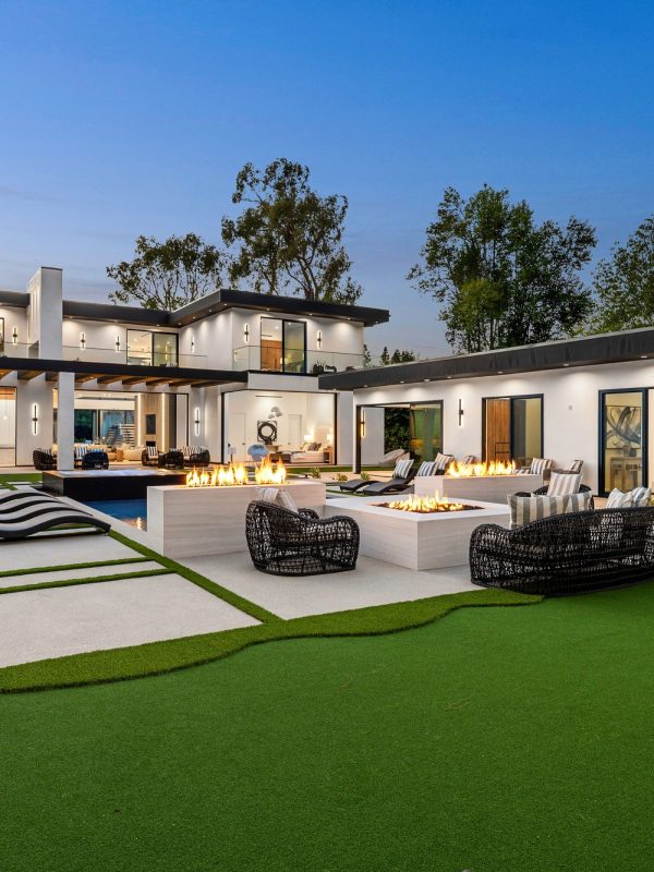 Modern luxury home with backyard and fire pit at dusk.